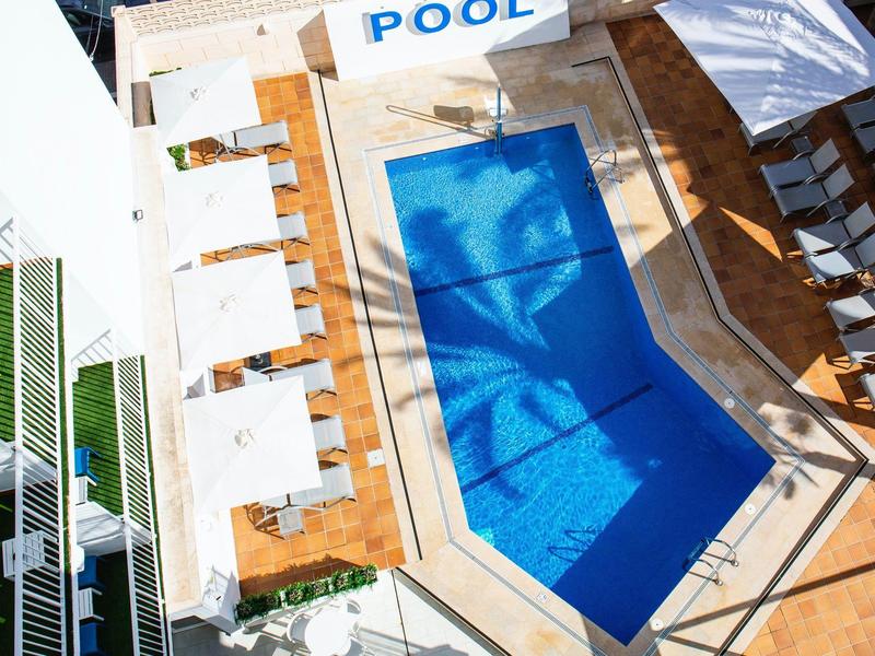 Terraza en la azotea con piscina azul y tumbonas bajo sombrillas blancas.
