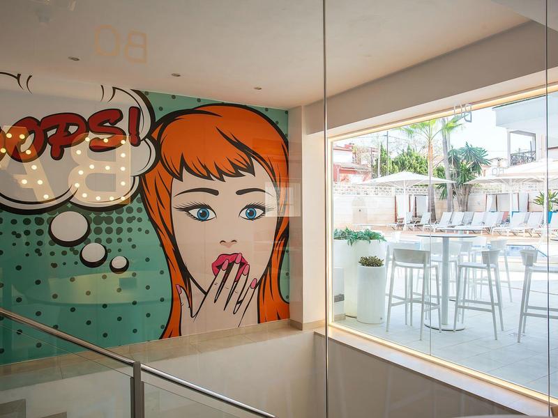 Colorido mural con mujer de cómic y bocadillo 'Oops!' en un moderno lobby de hotel cerca de la terraza.