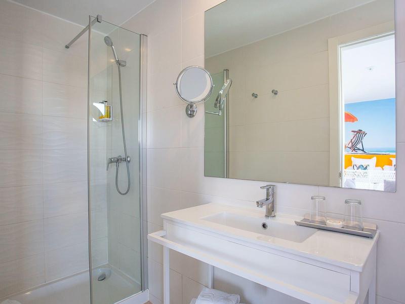 Baño luminoso con ducha de vidrio, espejo grande y lavabo blanco con grifo.