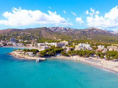 Piaszczysta plaża z niebieską wodą i górami w tle pod częściowo pochmurnym niebem.