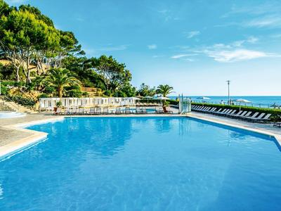 Piscine extérieure au bord de la mer avec chaises longues et arbustes verts.