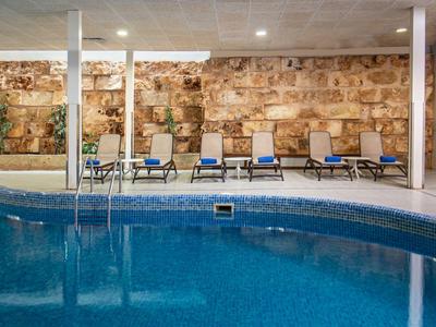 Kryty basen z leżakami i kamienną ścianą.