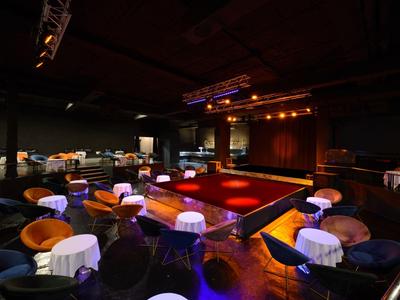 Spazio eventi elegante con palco, tavoli rotondi e sedie comode sotto un'illuminazione calda.