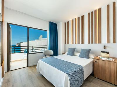 Camera d'hotel moderna con letto matrimoniale, balcone e vista mare alla luce del giorno.