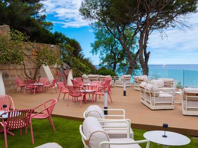 Taras z miejscami do siedzenia, widokiem na morze i pochmurne niebo w ogrodzie hotelowym.