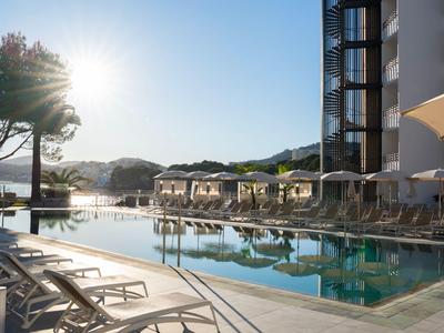 Nowoczesny basen na zewnątrz z leżakami i parasolami obok hotelu o zachodzie słońca.