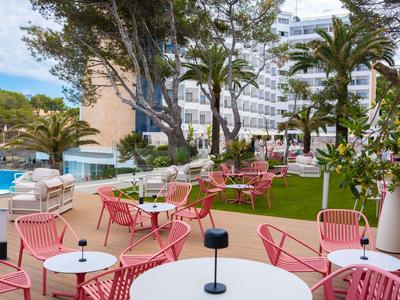 Taras z czerwonymi krzesłami i stołami obok basenu i budynku hotelu z palmami