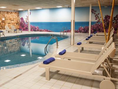 Kryty basen z białymi leżakami, niebieskimi ręcznikami i dekoracyjnymi malowidłami ściennymi.