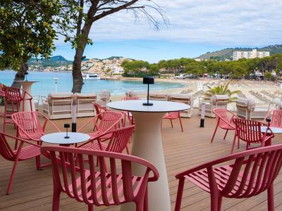 Czerwony zewnętrzny obszar siedzący z widokiem na piaszczystą plażę i czystą wodę pod pochmurnym niebem.