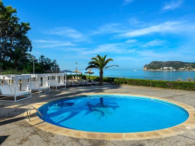 Okrągły basen z czystą wodą i palmami przy morzu pod niebieskim niebem.