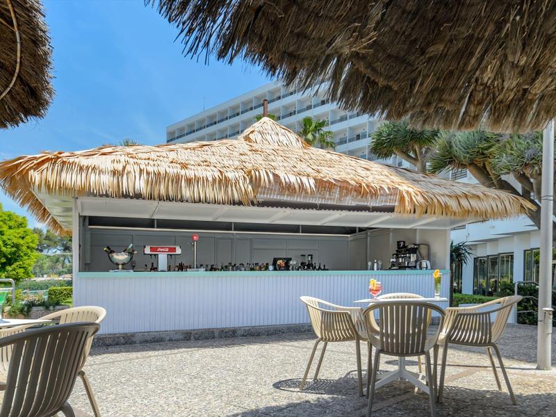 Otwarty bar z krzesłami i parasolami z trzciny pod jasnoniebieskim niebem.