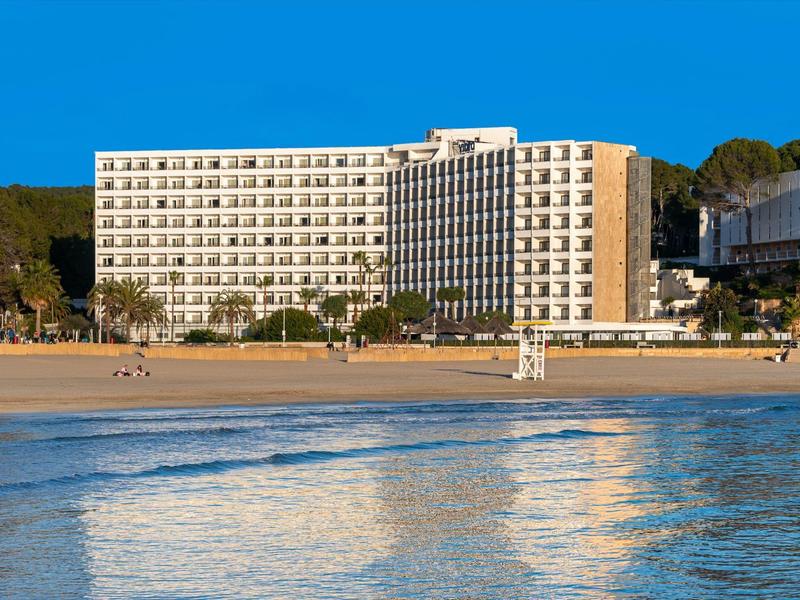 Nowoczesny hotel z widokiem na piaszczystą plażę pod niebieskim niebem.