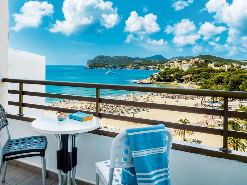 Balkon z stołem i krzesłami z widokiem na zatłoczoną plażę i morze pod błękitnym niebem.