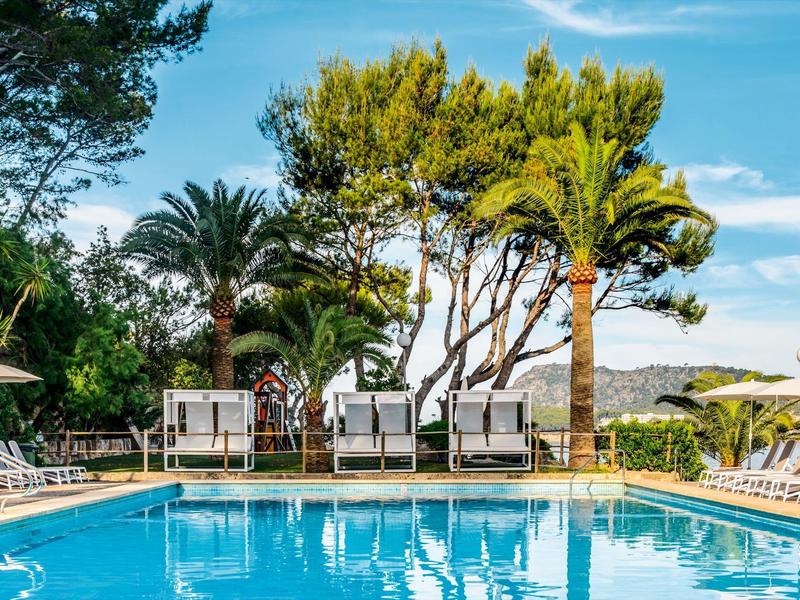 Otwarty basen otoczony leżakami i palmami pod niebieskim niebem.