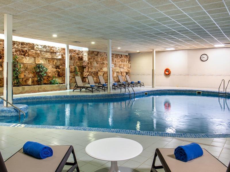 Basen kryty z leżakami i kamienną ścianą dekoracyjną.