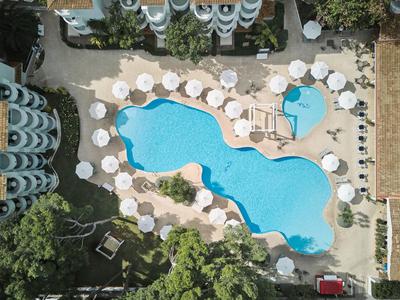 Widok z lotu ptaka na hotelowy basen z białymi parasolami i leżakami.