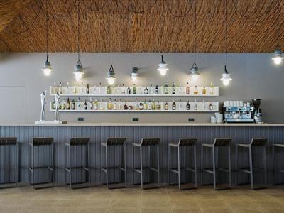 Nowoczesny bar hotelowy z szarymi stołkami barowymi i półkami na butelki pod drewnianym sufitem.