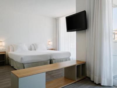 Jasny pokój hotelowy z dwoma łóżkami, telewizorem z płaskim ekranem i dużym oknem z zasłonami.