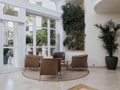 Elegancki kącik wypoczynkowy z dwoma fotelami i sofą przed dużymi oknami i roślinami.