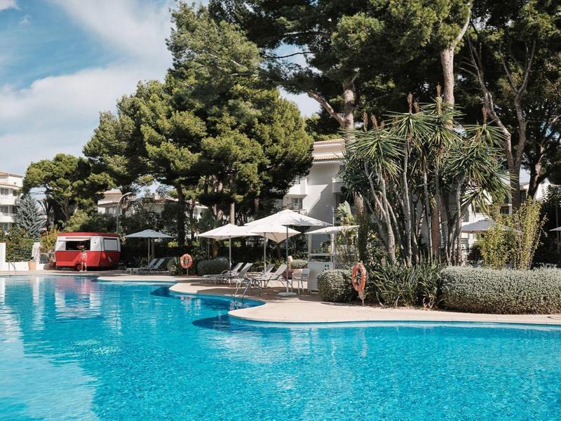 Duży basen z czystą wodą otoczony drzewami i meblami basenowymi pod niebieskim niebem.