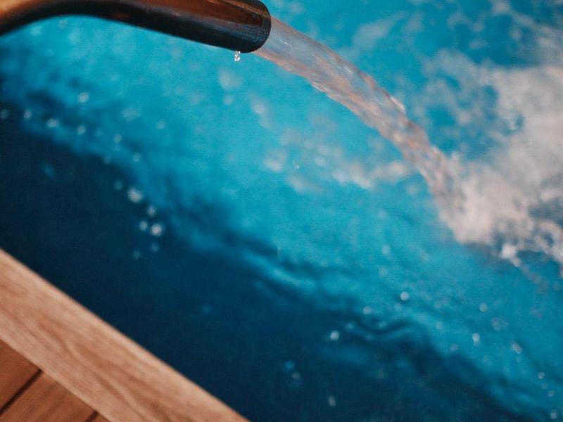 Woda płynie ze złotego kranu do niebieskiego basenu z drewnianym tarasem