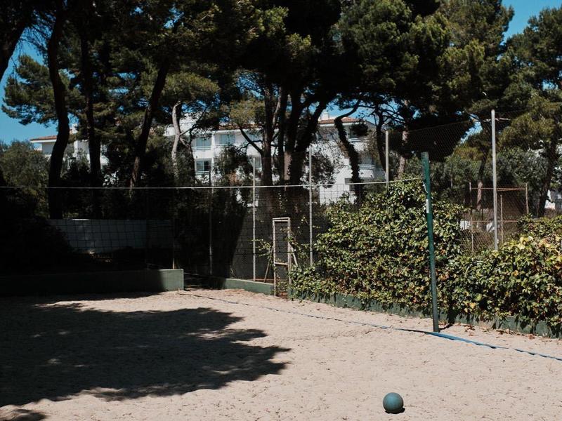 Piaszczyste boisko z grą w kręgle przed drzewami i domem pod czystym niebem.