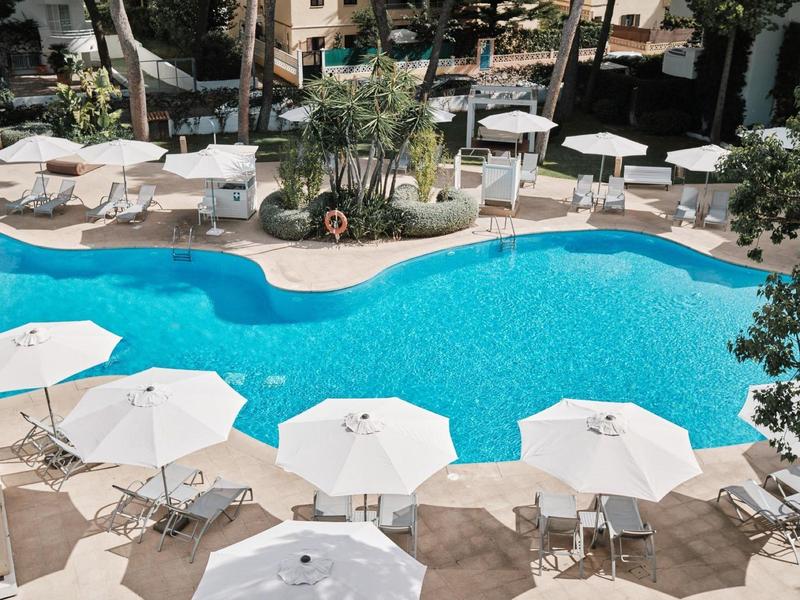 Basen hotelowy z niebieską wodą otoczony parasolami i leżakami w słoneczny dzień