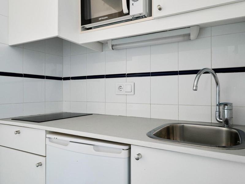 Mała nowoczesna kuchnia z zlewem, płytą grzewczą i wbudowaną mikrofalówką.