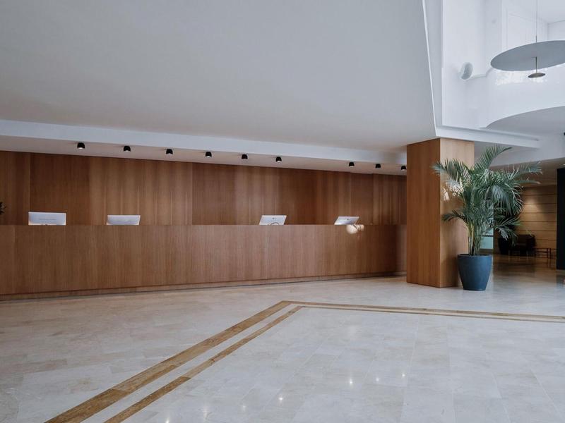 Jasne lobby hotelowe z długim drewnianym kontuar i dużą marmurową podłogą.