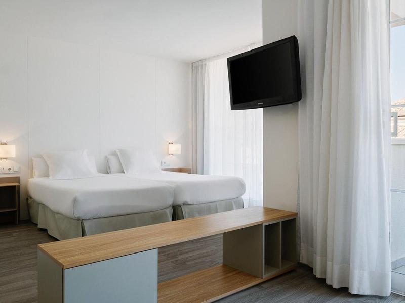 Jasny pokój hotelowy z dwoma łóżkami, telewizorem z płaskim ekranem i dużym oknem z zasłonami.