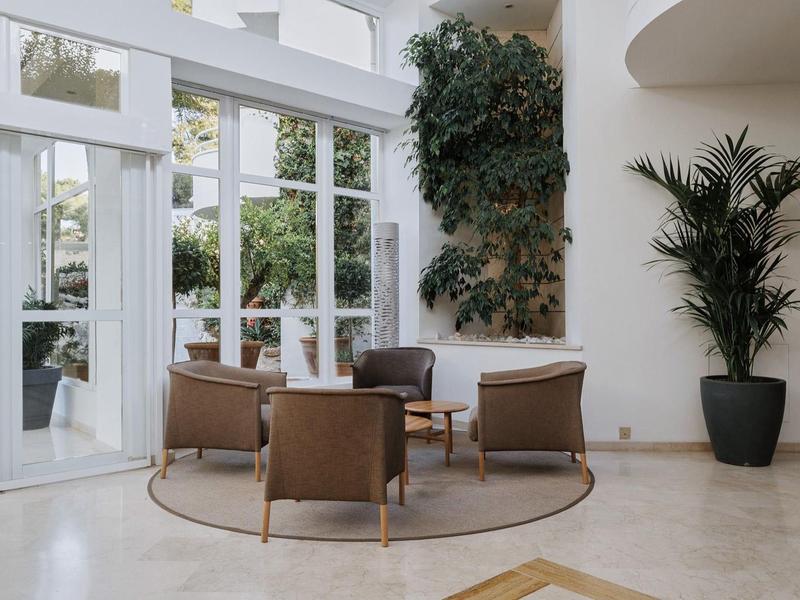 Elegancki kącik wypoczynkowy z dwoma fotelami i sofą przed dużymi oknami i roślinami.