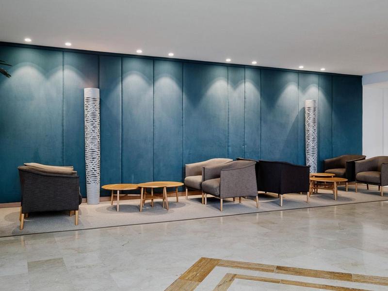 Nowoczesny hotelowy salon z fotelami, sofami i drewnianymi stolikami na tle niebieskiej ściany.