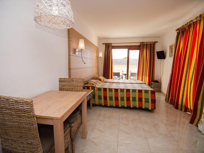 Hotelzimmer mit Doppelbett, bunten Vorhängen, Sitzbereich und Meerblick durch Fenster.