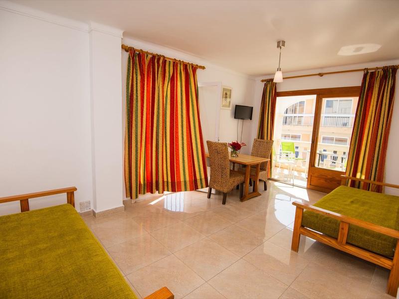 Helles Hotelzimmer mit zwei Betten, Tisch, Stühlen und großen Fenstern mit bunten Vorhängen