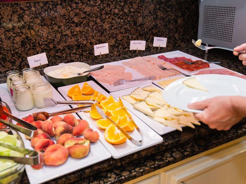 Buffet mit frischem Obst und Wurstscheiben, Person nimmt sich Essen auf einen Teller