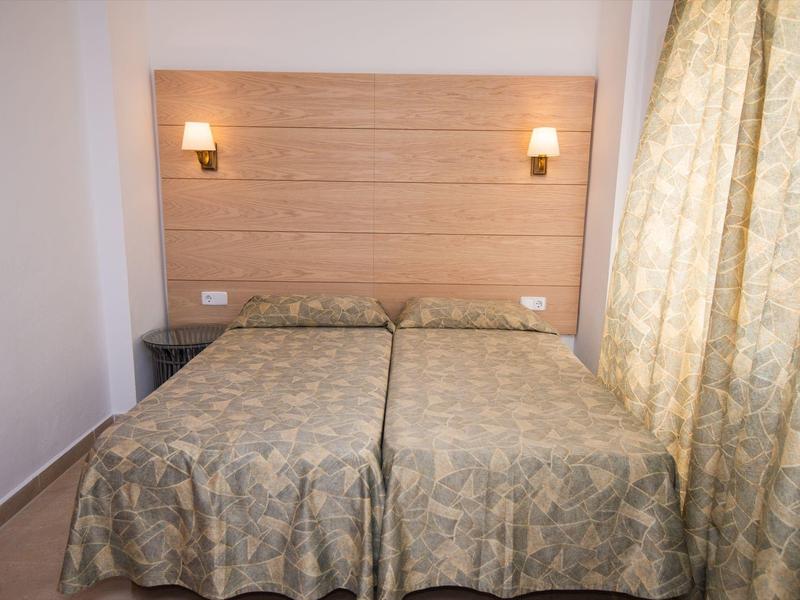 Zwei Einzelbetten mit identischer Bettwäsche und Holzkopfteil in einem hellen Hotelzimmer