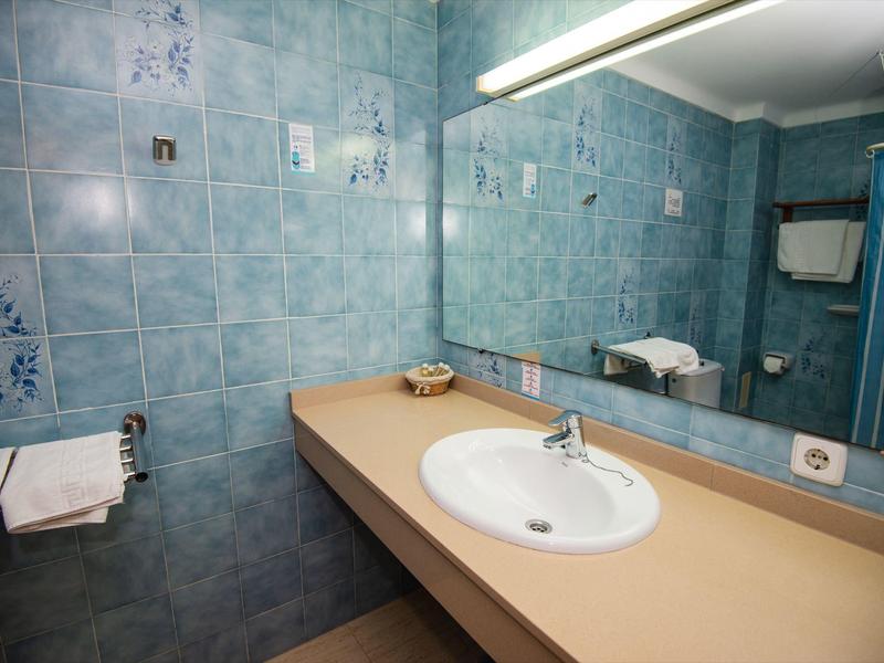 Badezimmer mit blau gekachelten Wänden, einem großen Spiegel und einem Waschbecken auf einer hellen Arbeitsplatte.