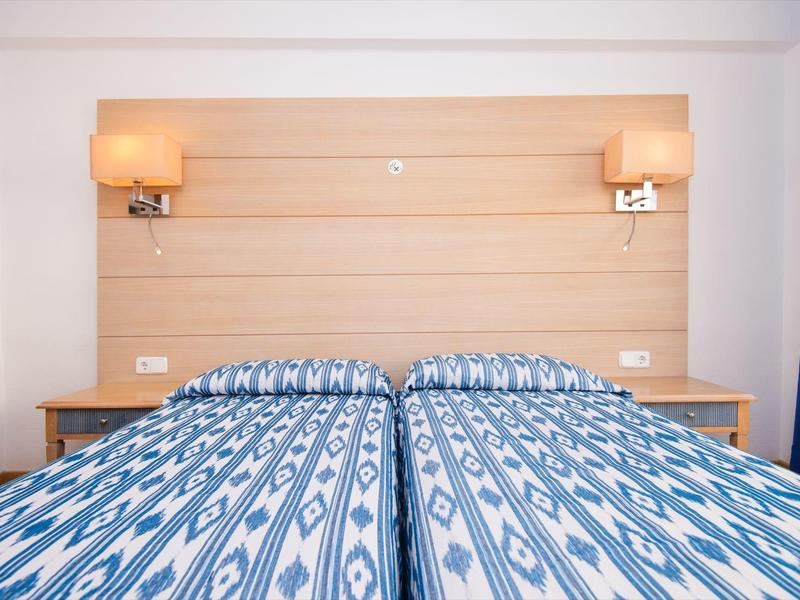 Zwei Einzelbetten mit blau gemusterten Decken und einem gemeinsamen Holzkopfteil mit Wandlampen.