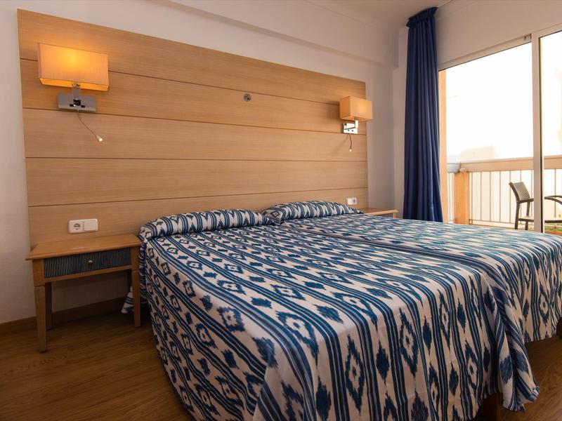 Hotelzimmer mit Einzelbett, blau gemustertem Bettbezug, Holzvertäfelung und Balkon mit Geländer