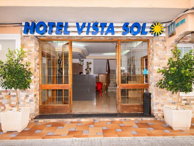 Eingang eines Hotels mit offenem Holztüren und zwei großen Pflanzen in weißen Töpfen