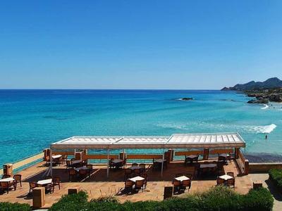 Wide beach view with blue sea, sun loungers, umbrellas, and a clear sky.