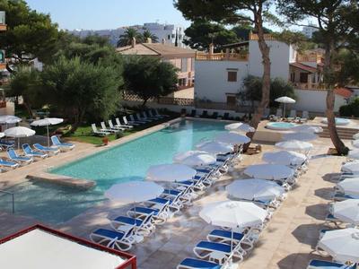 Outdoor hotel pool with lounge chairs under clear blue sky and trees around.