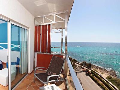 Hotel room with two beds and balcony overlooking the clear sea and rocky shoreline.