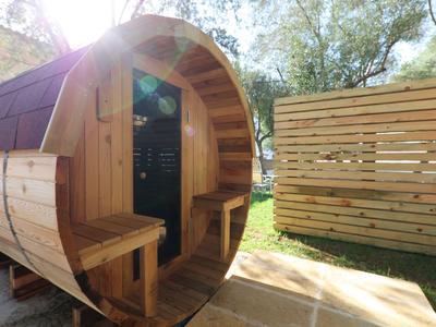 Round wooden sauna house with doors and benches, next to a wooden fence in the garden.