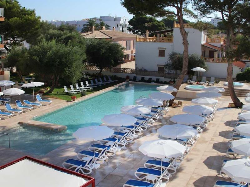 Outdoor hotel pool with lounge chairs under clear blue sky and trees around.