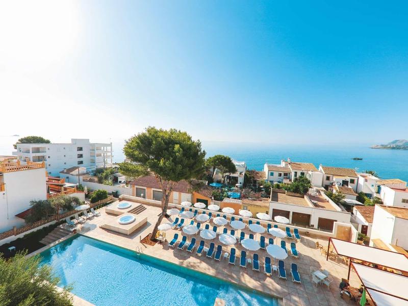 Sunny hotel terrace with swimming pool, sun loungers, and sea view under clear blue sky.