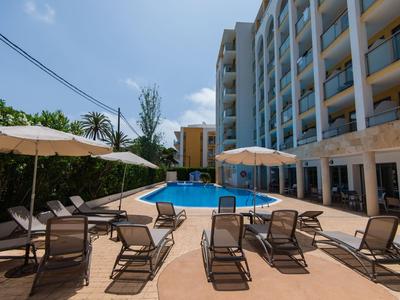 Hotelpoolbereich mit Liegestühlen und Sonnenschirmen neben einem mehrstöckigen Gebäude.