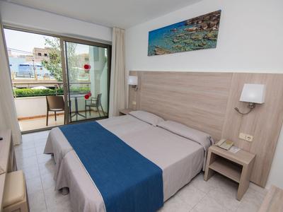 Modernes Hotelzimmer mit Doppelbett, blauem Bettläufer und Balkon mit Gartenblick.
