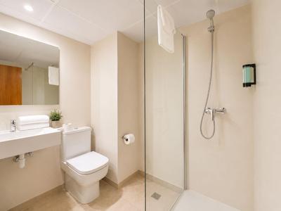 Helle Hotelbadezimmer mit Toilette, Waschbecken und begehbarer Dusche in neutralen Tönen.