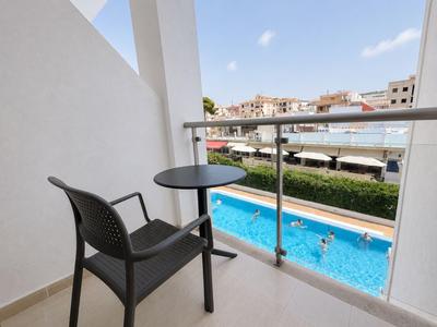 Balkon mit schwarzem Stuhl und Tisch bietet Blick auf Pool und umliegende Häuser.